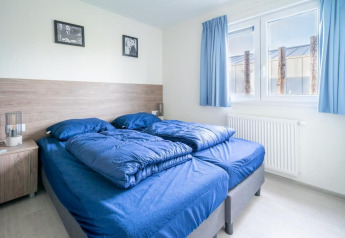 Lichte slaapkamer met twee blauwe eenpersoonsbedden, grote ramen en blauwe gordijnen in Pavilion Waterfront 8.