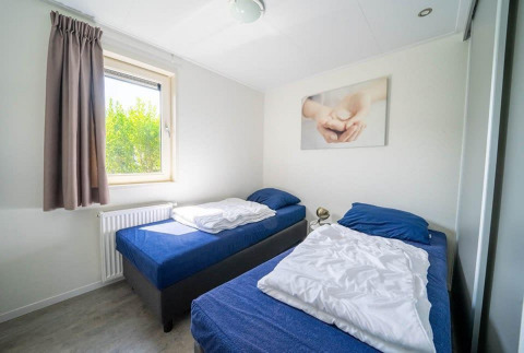 Lichte kamer in Pavilion Waterfront 8 aan De Kraaijenbergse Plassen met twee bedden en een groot raam.