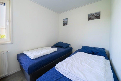 Habitación con dos camas individuales, ropa de cama azul, paredes blancas y cuadros en Pavilion Waterfront 8.
