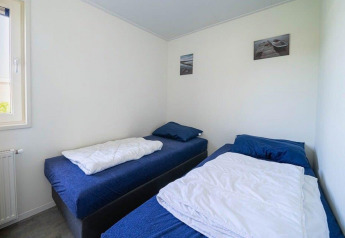 Camera con due letti singoli, biancheria blu, pareti bianche e quadri presso Pavilion Waterfront 8, Paesi Bassi.