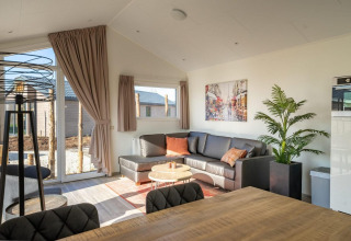 Lichte woonkamer met hoekzetel, grote kamerplant en veel ramen in Velthorst 4 lodge, Nederland.