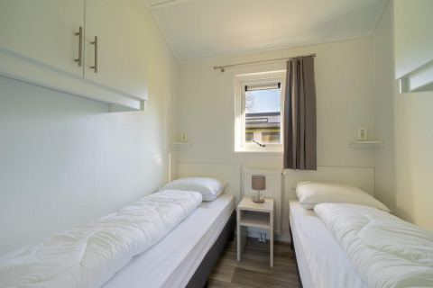 Chambre lumineuse avec deux lits simples, une table de nuit et une fenêtre à Velthorst 4, De Kraaijenbergse Plassen, Pays-Bas.