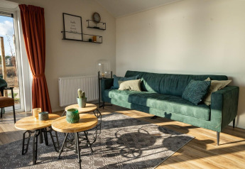 Moderne lodge woonkamer met groene zetel, ronde houten tafels, rode gordijnen en veel natuurlijk licht.