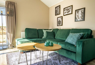 Modernes Lodge-Wohnzimmer mit grüner Eckcouch, runden Holztischen, Vorhängen und Wandfotos.