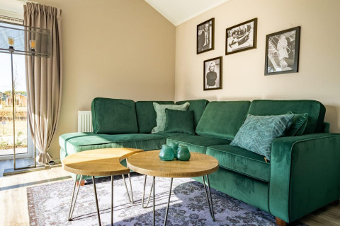 Moderne lodge-stue med grøn sofa, to runde træborde, et stort vindue og sort-hvide billeder på væggen.