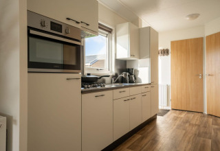 Cocina moderna en una cabaña con suelo de aspecto madera, horno empotrado, cocina de gas y armarios blancos.