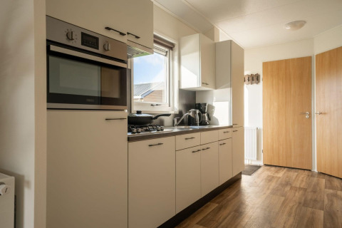 Cocina moderna en una cabaña con suelo de aspecto madera, horno empotrado, cocina de gas y armarios blancos.