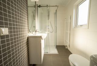 Baño moderno en una cabaña con ducha de vidrio, doble lavabo, inodoro y ventana grande.