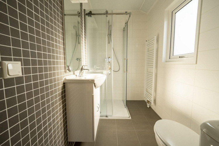 Baño moderno en una cabaña con ducha de vidrio, doble lavabo, inodoro y ventana grande.