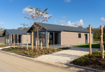 Moderne lodge met houten bekleding en grote ramen, omringd door tuin en blauwe hemel.