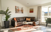 Moderne stue i en lodge med hjørnesofa, kunst på væggen, grøn plante og store vinduer med gardiner.