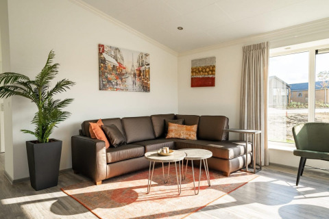 Moderne stue i en lodge med hjørnesofa, kunst på væggen, grøn plante og store vinduer med gardiner.