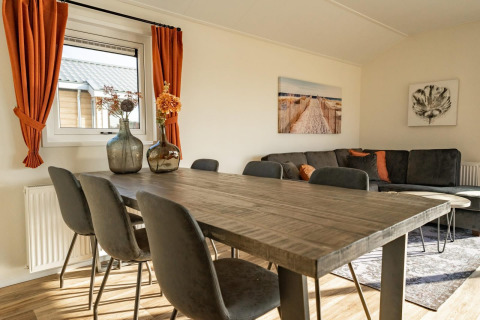 Luminoso salón de lodge con mesa de madera, sillas oscuras, cortinas naranjas y arte en la pared.