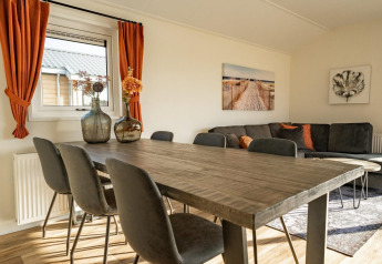 Lichte lodge woonkamer met houten tafel, zwarte stoelen, oranje gordijnen en moderne muurdecoratie.