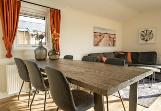 Lyst opholdsrum i en lodge med træbord, sorte stole, orange gardiner og moderne vægkunst.