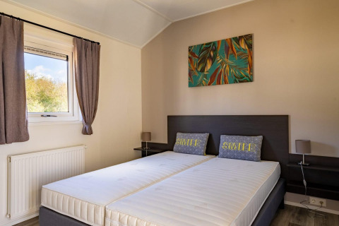 Modernes Schlafzimmer mit zwei Einzelbetten, Kissen mit 'SMILE' Schriftzug und farbigem Wandbild.