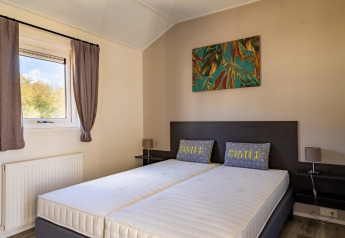Moderne lodge slaapkamer met twee eenpersoonsmatrassen, kussens met 'SMILE' en een fel muurschilderij.