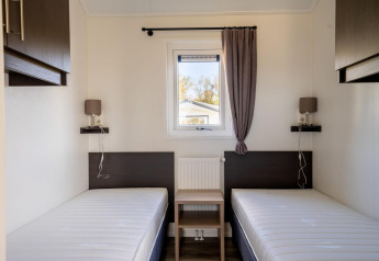 Minimalistische lodgekamer met twee enkele bedden, centraal raam en modern donker meubilair.