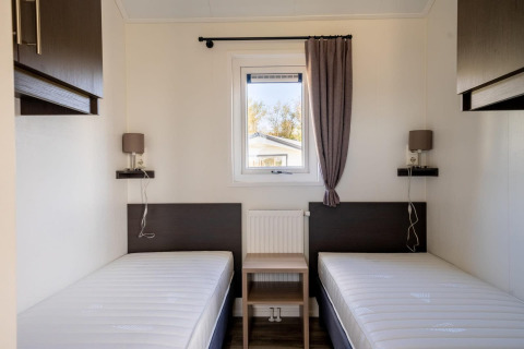 Minimalistisk lodge-værelse med to enkeltsenge, et vindue i midten, og moderne brune møbler.