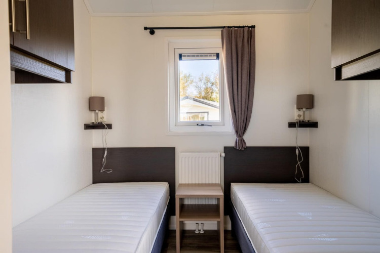 Habitación minimalista de lodge con dos camas individuales, ventana central y muebles modernos.