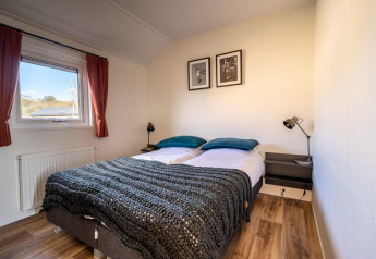 Lichte lodgekamer met dubbel bed, nachtkastjes, leeslampen, raam en houten vloer.