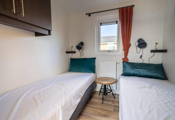 Moderne lodgeværelse med to enkeltsenge, grønne puder, lille træbord og vindue med rød gardin.