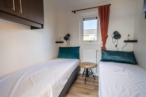 Habitación de lodge moderna con dos camas individuales, almohadas verdes, mesa pequeña y ventana con cortina.