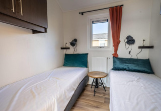 Moderne lodgeværelse med to enkeltsenge, grønne puder, lille træbord og vindue med rød gardin.