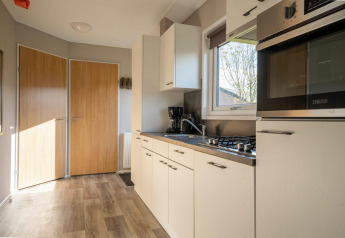Moderne lodgekeuken met witte kasten, houten deuren, fornuis, oven en helder raam met uitzicht.