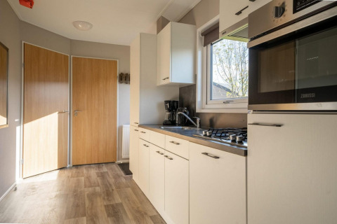 Cocina moderna en una cabaña con puertas de madera, armarios blancos, horno, fogón y ventana luminosa.