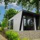 Moderne lodge ved navn Just Nature omgivet af grønne træer og planter, set på en solrig dag
