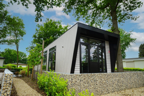 Moderne lodge ved navn Just Nature omgivet af grønne træer og planter, set på en solrig dag