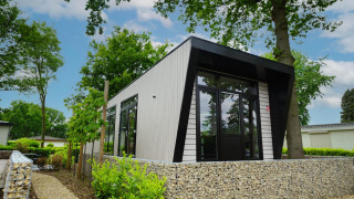 Moderne lodge ved navn Just Nature omgivet af grønne træer og planter, set på en solrig dag