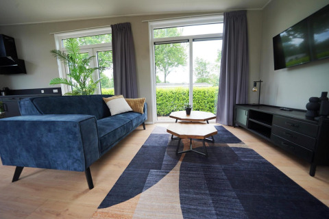 Salón moderno en Just Nature Lodge, Limburg, Países Bajos, sofá azul, grandes ventanas y vista al jardín.