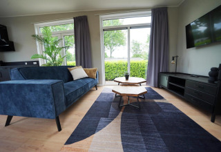 Salón moderno en Just Nature Lodge, Limburg, Países Bajos, sofá azul, grandes ventanas y vista al jardín.