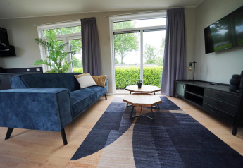 Moderne woonkamer bij Just Nature Lodge, Limburg, Nederland, blauwe zetel, grote ramen en tuinzicht.