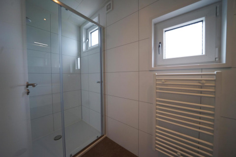 Doccia moderna con porta in vetro, pareti piastrellate bianche e termosifone vicino alla finestra a Limburg.