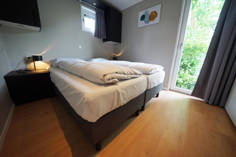 Moderne slaapkamer in de Just Nature lodge in Limburg, Nederland met twee bedden en uitzicht op groen.