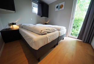 Moderne lodge soveværelse på Just Nature i Limburg, Holland med to senge, trægulv og udsigt til natur.