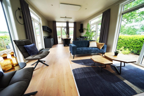 Interno di una moderna lodge Just Nature a Limburg, Paesi Bassi, con grandi finestre e arredi eleganti.