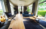 Moderne lodge i Limburg, Holland, med store vinduer, blå sofa, stole og naturlig udsigt.