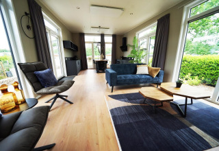 Interno di una moderna lodge Just Nature a Limburg, Paesi Bassi, con grandi finestre e arredi eleganti.