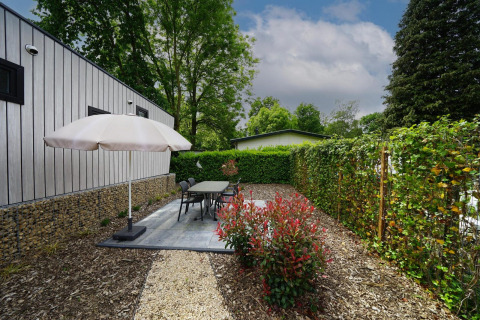 Patio esterno al lodge Just nature a Limburg, Paesi Bassi, con ombrellone, tavolo e siepi verdi.