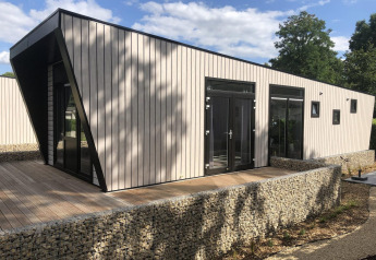 Moderne lodge med unikt design på Just Nature i Limburg, Holland, omgivet af træer og blå himmel.