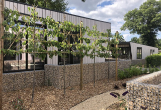 Lodge contemporaneo a Just Nature, Limburg, Paesi Bassi, con muri di pietra e sentiero nel giardino.