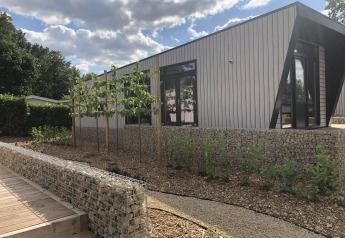Moderne lodge ved Just Nature i Limburg, Holland, omgivet af grønne planter, stenvægge og blå himmel.