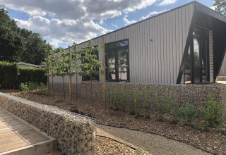 Lodge moderno Just Nature en Limburg, Países Bajos, rodeado de vegetación, paredes de piedra y cielo azul.