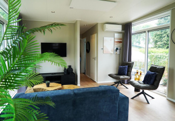 Moderne woonkamer in Just Nature Lodge te Limburg, Nederland, met grote ramen, blauwe zetel en planten.