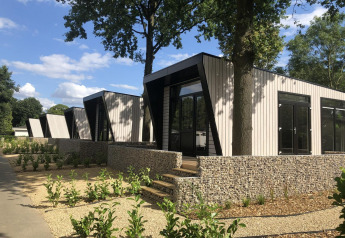 Moderne lodge Just Nature te Limburg, Nederland, omringd door groen en steenmuren onder blauwe hemel.