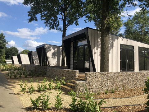 Moderne lodge Just Nature te Limburg, Nederland, omringd door groen en steenmuren onder blauwe hemel.